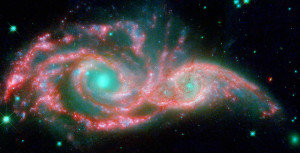 These shape-shifting galaxies have taken on the form of a giant mask. The icy blue eyes are actually the cores of two merging galaxies, called NGC 2207 and IC 2163, and the mask is their spiral arms. The false-colored image consists of infrared data from NASA's Spitzer Space Telescope (red) and visible data from NASA's Hubble Space Telescope (blue/green).   NGC 2207 and IC 2163 met and began a sort of gravitational tango about 40 million years ago. The two galaxies are tugging at each other, stimulating new stars to form. Eventually, this cosmic ball will come to an end, when the galaxies meld into one. The dancing duo is located 140 million light-years away in the Canis Major constellation.  The infrared data from Spitzer highlight the galaxies' dusty regions, while the visible data from Hubble indicates starlight. In the Hubble-only image (not pictured here), the dusty regions appear as dark lanes.  The Hubble data correspond to light with wavelengths of .44 and .55 microns (blue and green, respectively). The Spitzer data represent light of 8 microns.